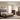 A coordinated bedroom furniture set in a warm wood finish, including a bed frame with headboard and footboard, a nightstand, a tall chest, a dresser with mirror, and matching lamps, arranged in a styled room with beige walls, wood flooring, and neutral bedding.