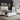 A modern bedroom furniture set in glossy white, featuring a bed with a cream upholstered headboard and blue LED lighting, a matching nightstand, a tall chest, a dresser with a mirror, and a drawer unit, all shown on a light gray background.