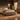 A rustic bedroom furniture set in a warm, styled room. The set includes a bed frame with a tall headboard, two matching nightstands, a chest of drawers, and a dresser with a matching mirror.