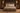 A rustic gray wooden bed frame with a high panel headboard and footboard, styled with beige and brown bedding, shams, and a textured throw blanket, set in a dark wood bedroom with matching nightstands and wall sconces.