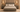 A rustic gray-brown wooden bed frame with a matching headboard and footboard, styled with neutral beige and white bedding, set in a symmetrical bedroom with matching nightstands and wall sconces.